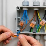 Dłonie łączą przewody elektryczne w otwartej puszce instalacyjnej za pomocą złączek sprężynowych